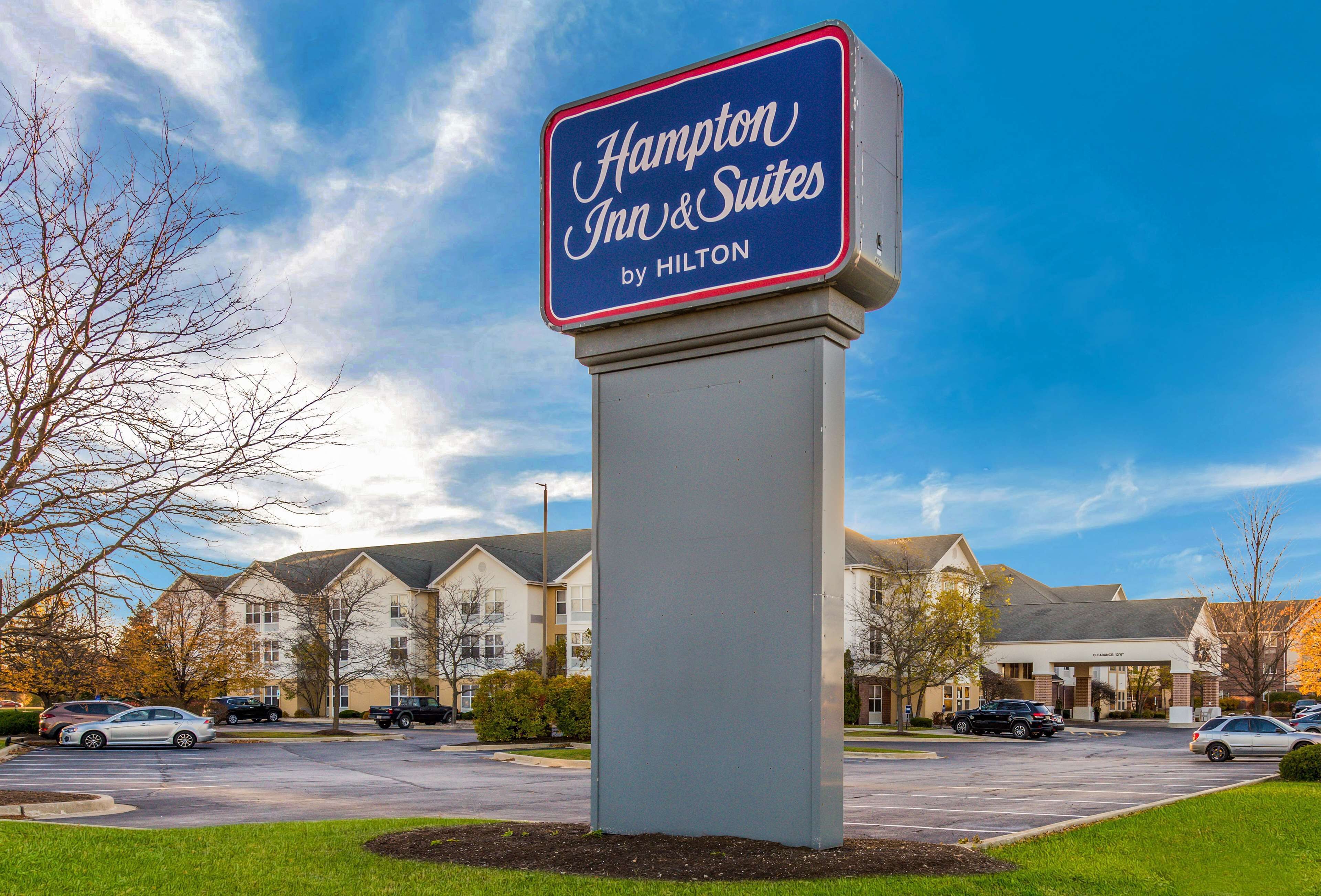 A Hampton Inn & Suites sign with a clear view of the hotel building in the background.