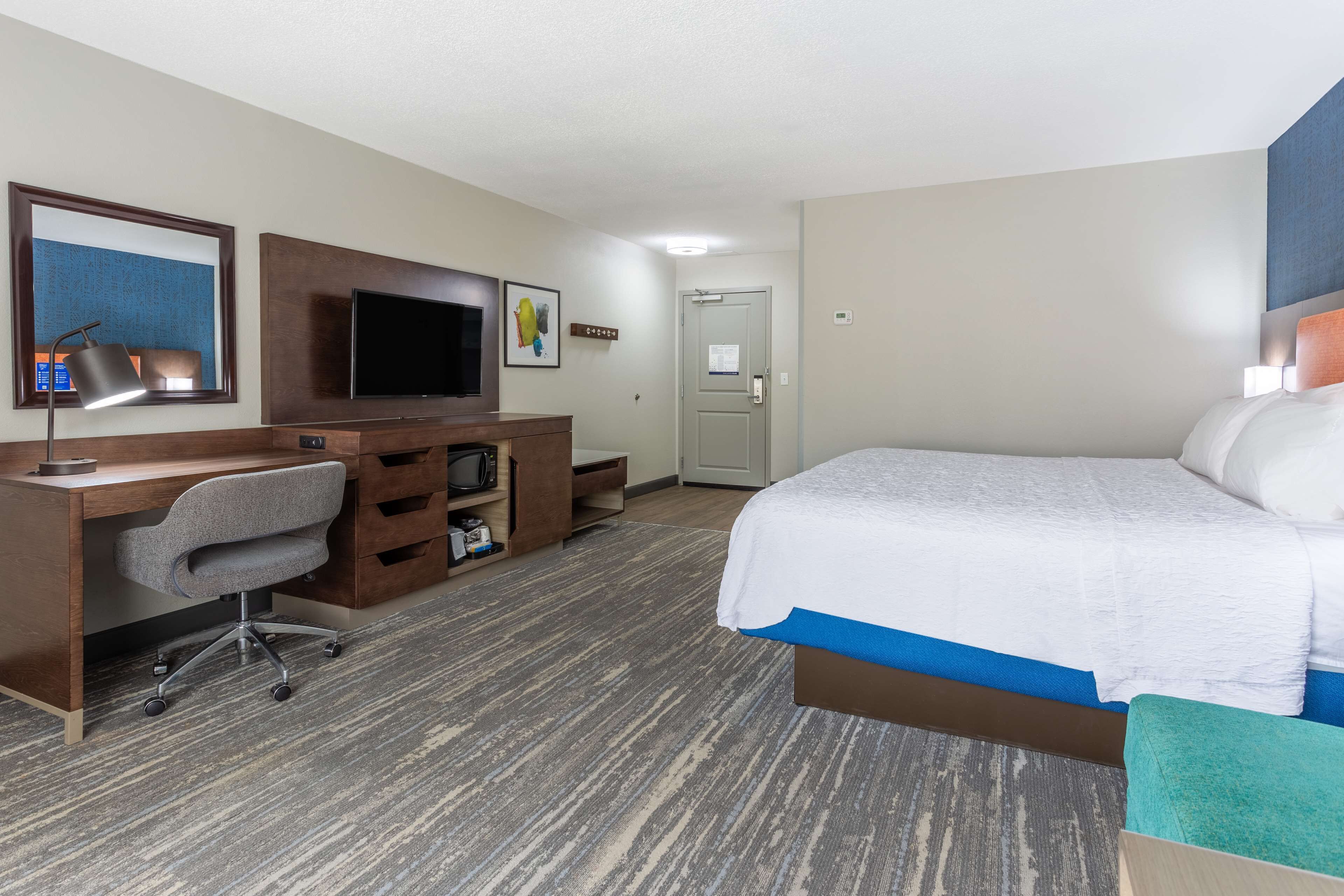 A hotel room with a bed, desk, chair, TV, and a door.