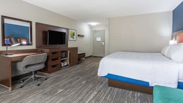 A hotel room with a bed, desk, chair, TV, and a door.