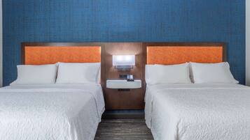 Habitación de hotel con dos camas, una mesita de noche con lámpara y un lavamanos en la pared.