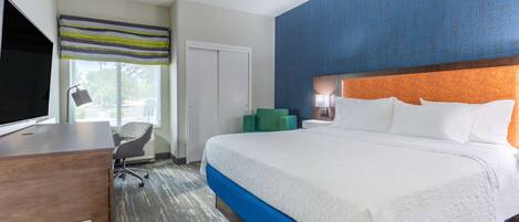 Ein Hotelzimmer mit einem großen Bett, einem Schreibtisch mit Fernseher, einem Sessel und einem Fenster mit Blick ins Freie.