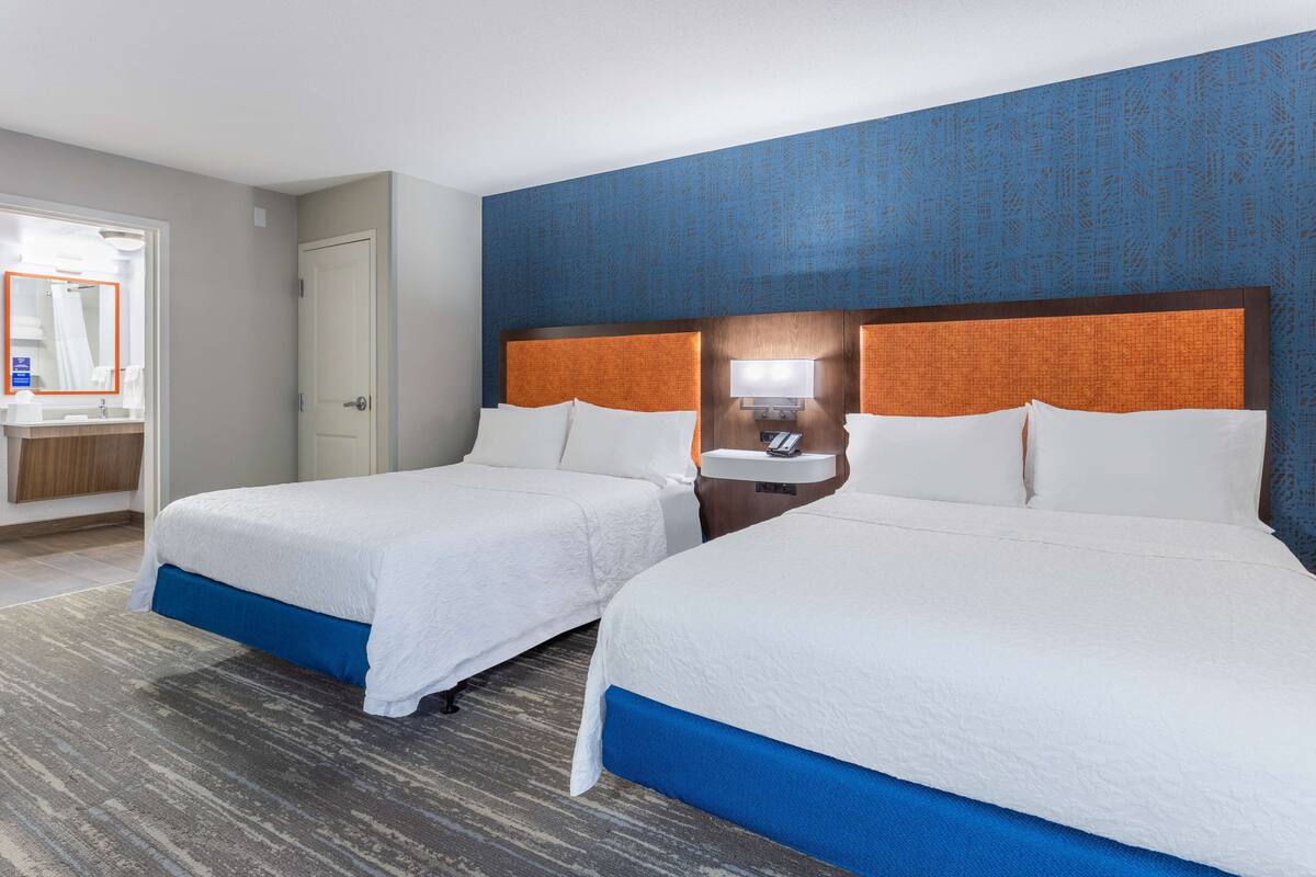 A hotel room with two beds, a bathroom, and a large mirror.