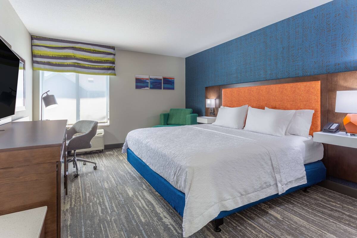 A hotel room with a large bed, a desk, a chair, and a window with a view.