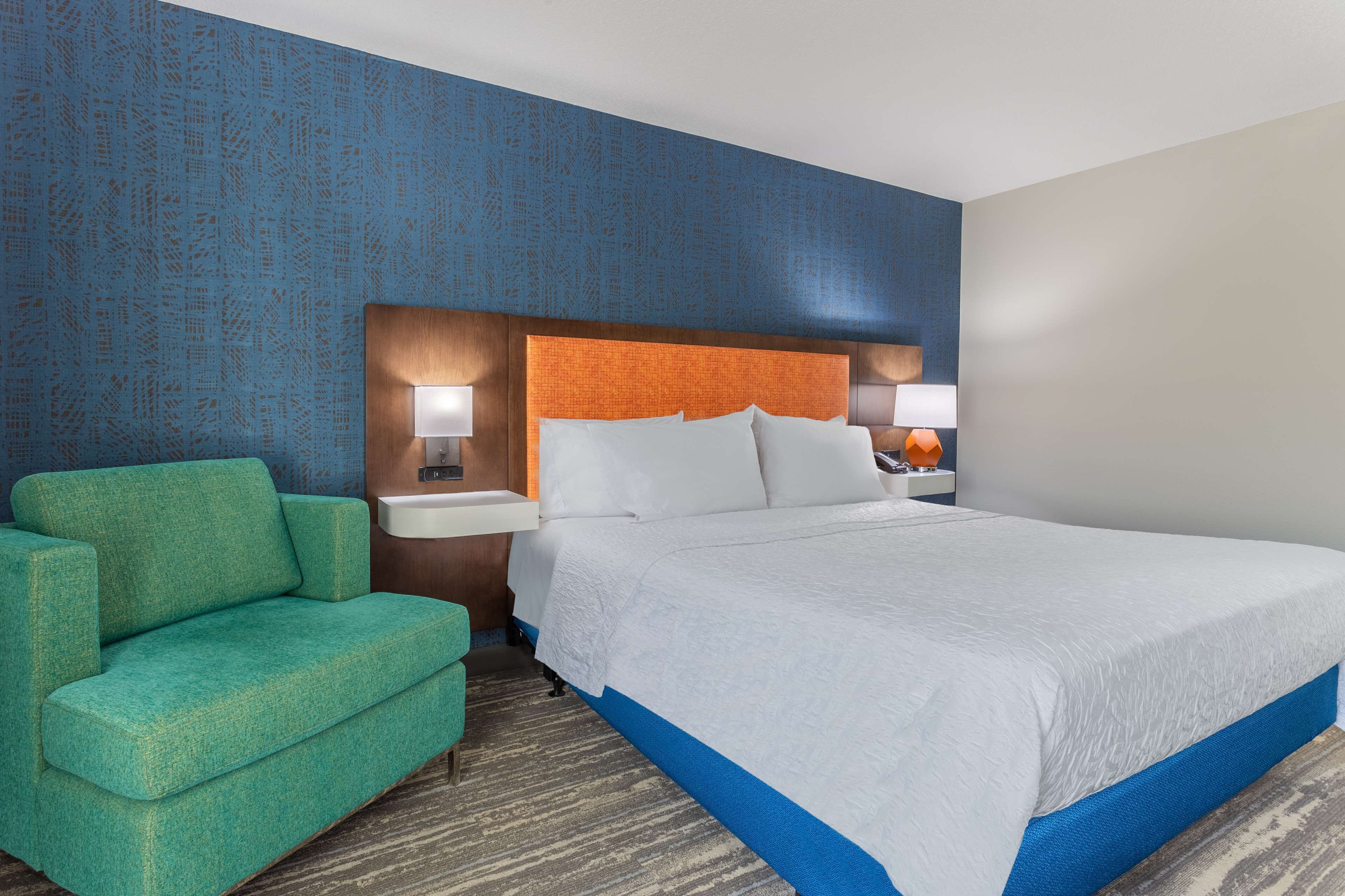 A hotel room with a large bed, a green armchair, and two bedside tables with lamps.