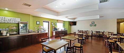 A spacious dining area with wooden tables and chairs, a kitchen counter with various appliances, and a green accent wall.