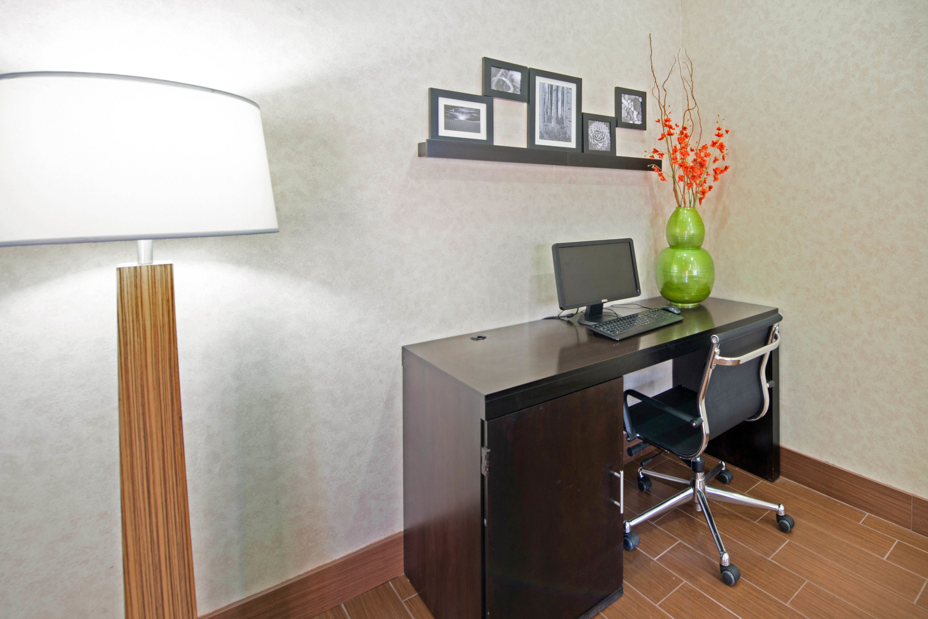 A modern office space with a desk, chair, lamp, and a vase with flowers.