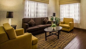Una sala de estar con un sofá marrón, un sillón amarillo y una mesa de centro. Hay dos lámparas sobre mesitas auxiliares y una planta sobre la mesa de centro.