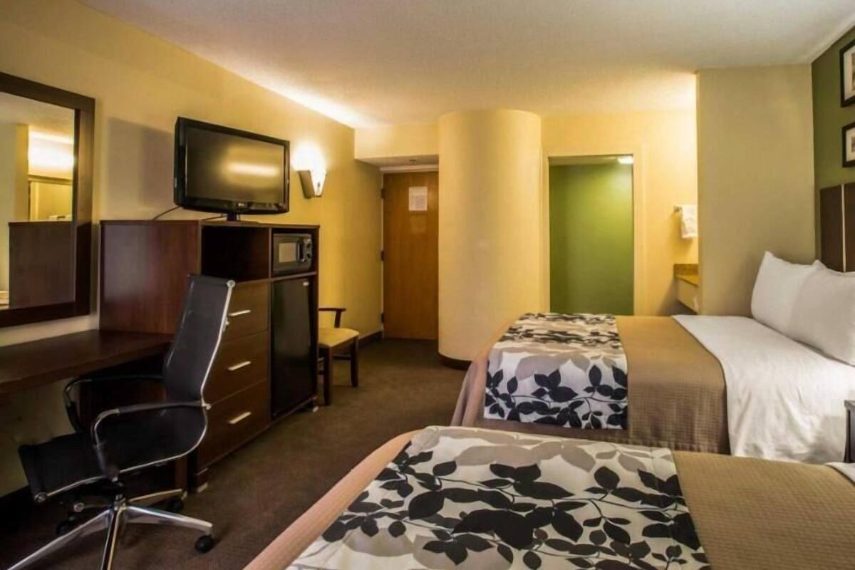 A hotel room with a desk, chair, television, two beds, and a door.