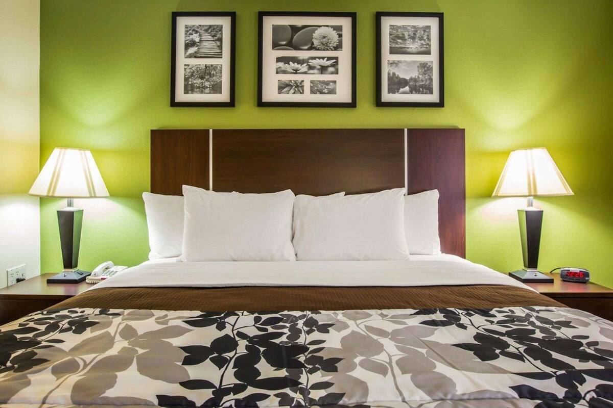 A hotel room with a bed, green walls, three framed pictures, two bedside lamps, and a floral-patterned bedspread.