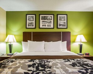 Une chambre d’hôtel avec un lit, des murs verts, trois tableaux encadrés, deux lampes de chevet et une couvre-lit à motifs floraux.