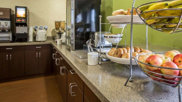 Un bufé de desayuno con una cafetera, un refrigerador y una exhibición de frutas.