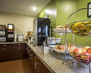 Un buffet de petit-déjeuner comprenant une machine à café, un réfrigérateur et un présentoir de fruits.
