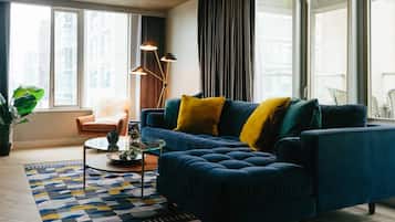A modern living room with a blue sofa, yellow cushions, a glass coffee table, and a patterned rug.