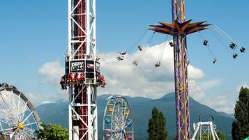 Une grande roue et des montagnes russes dans un parc d’attractions, avec des montagnes en arrière-plan.