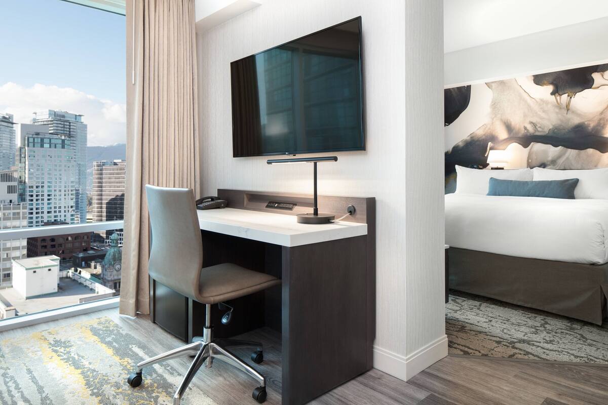 Una habitación de hotel con escritorio, silla, cama y televisor grande.