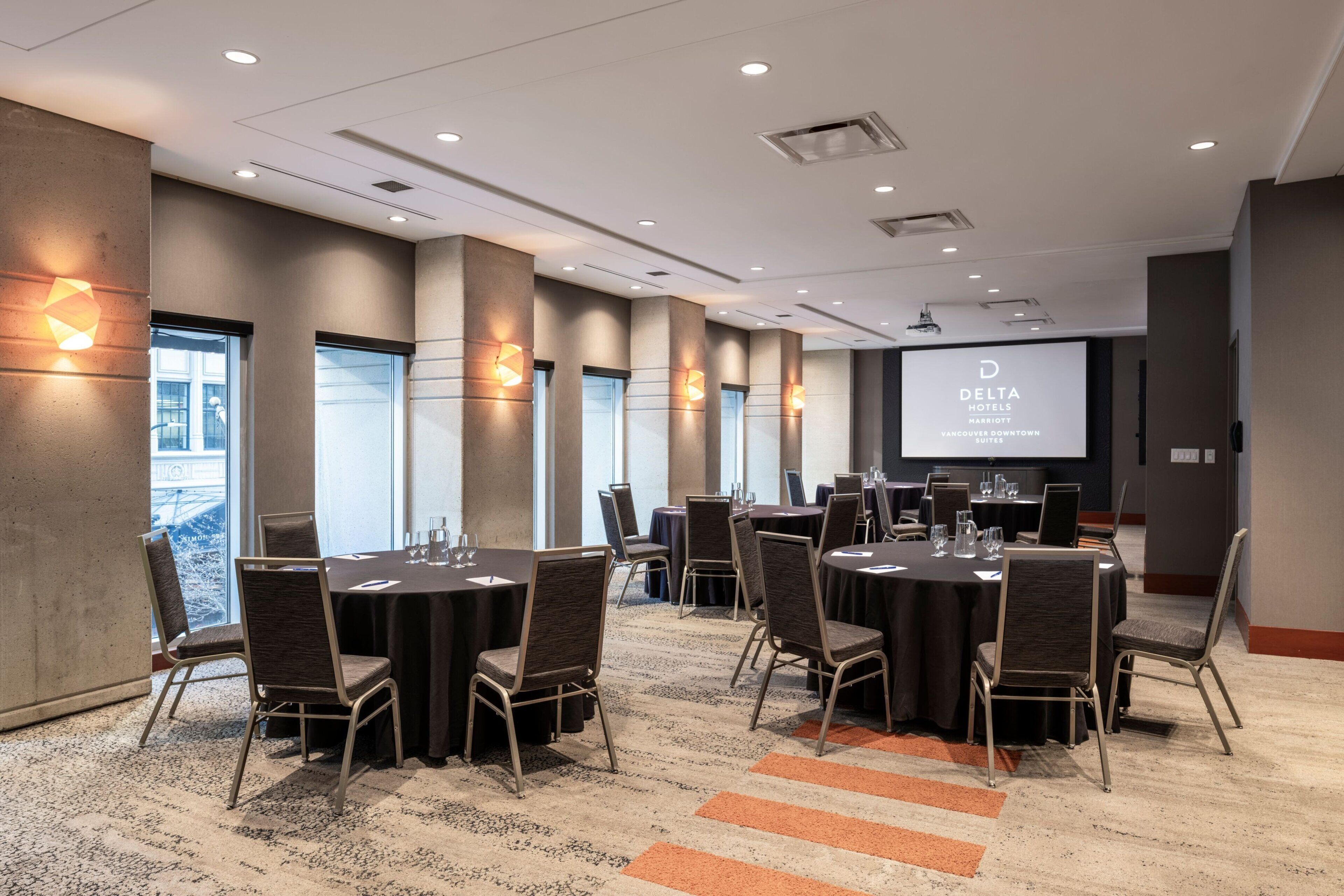 A conference room with round tables and chairs, a projector screen, and a large window.