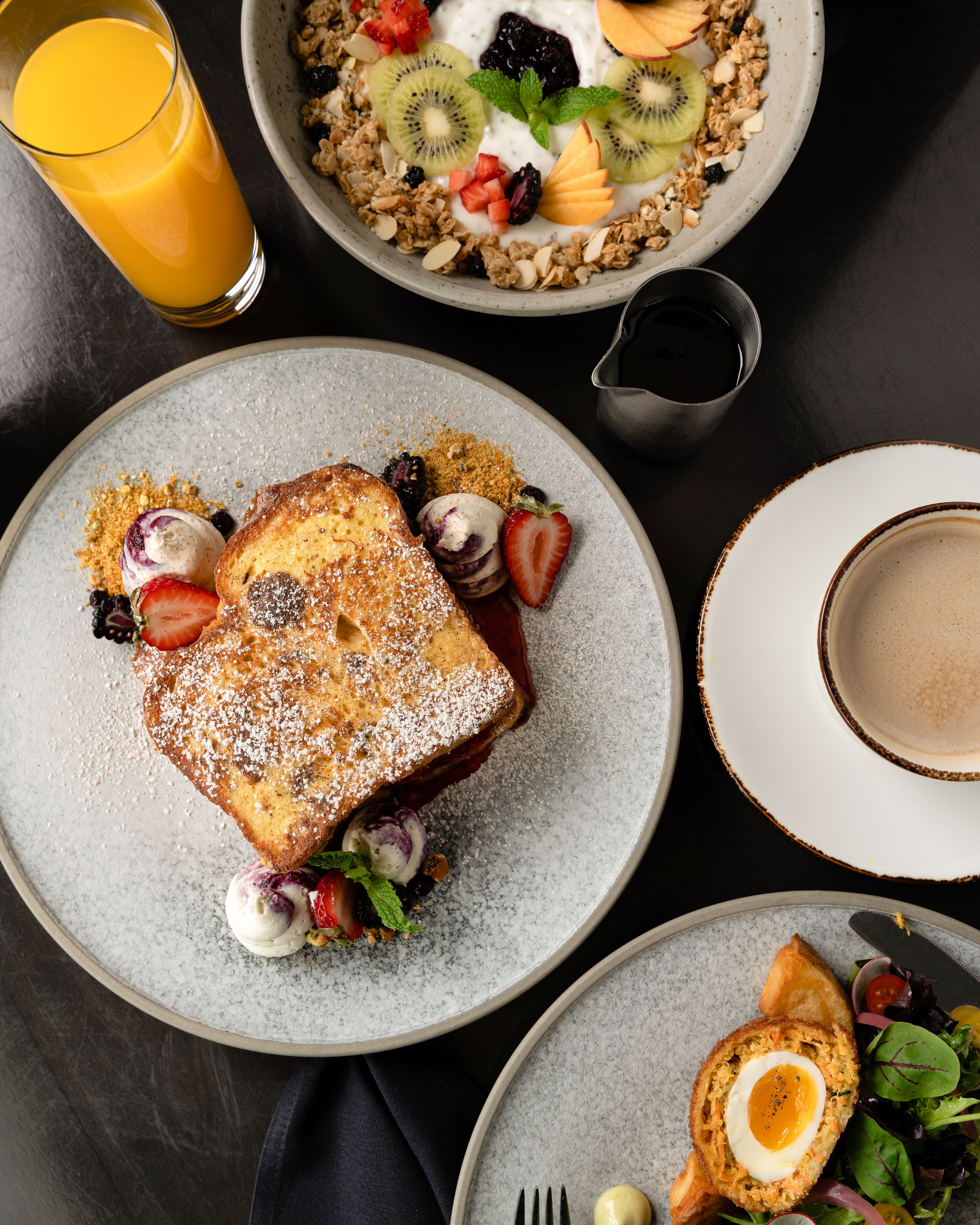 Une table dressée pour le petit-déjeuner, avec des toasts, des fruits, un yaourt et une tasse de café.