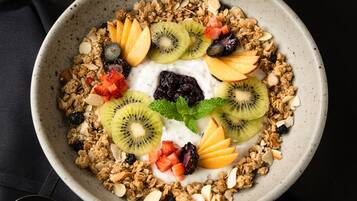 Un tazón de granola con frutas y nueces, un vaso de jugo de naranja y una taza de café sobre una mesa.