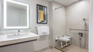 Un baño moderno con un espejo grande, un lavabo, un perchero para toallas y una zona de ducha con barra de apoyo.