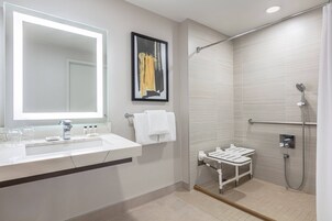Un baño moderno con un espejo grande, un lavabo, un perchero para toallas y una zona de ducha con barra de apoyo.