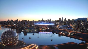 A city skyline at dusk with a large stadium and a spherical building near a waterfront.
