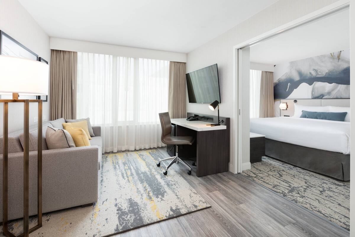 Habitación de hotel con cama, escritorio con computadora, silla, sofá y televisor.