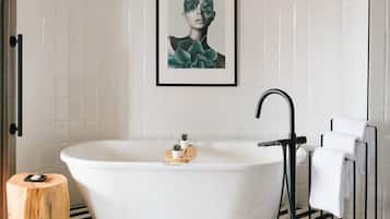 A modern bathroom with a freestanding bathtub, a framed artwork on the wall, and a towel rack with white towels.