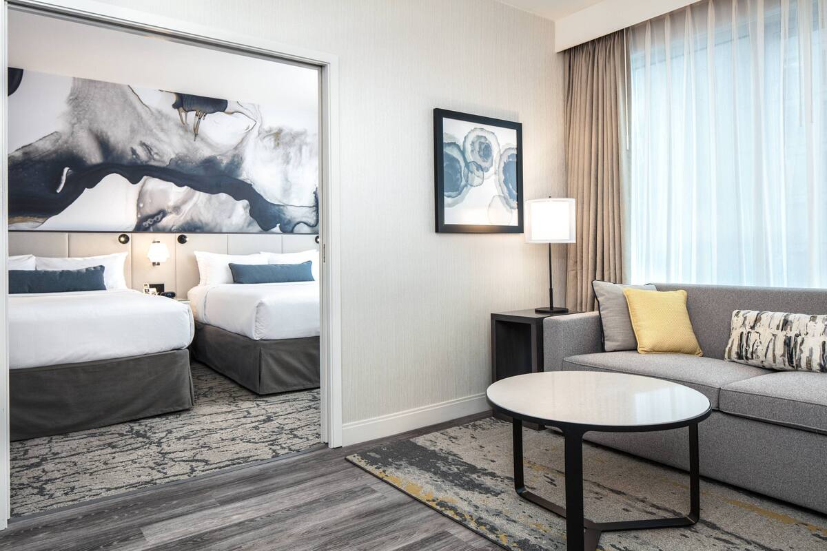 Habitación de hotel con dos camas, un sofá, una mesita redonda y un cuadro abstracto grande en la pared.