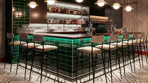 Eine Bar mit einer grün gefliesten Theke, mehreren Hockern sowie einer Auswahl an Flaschen und Gläsern.