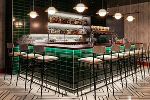 A bar area with a green-tiled bar counter, multiple stools, and a variety of bottles and glasses.