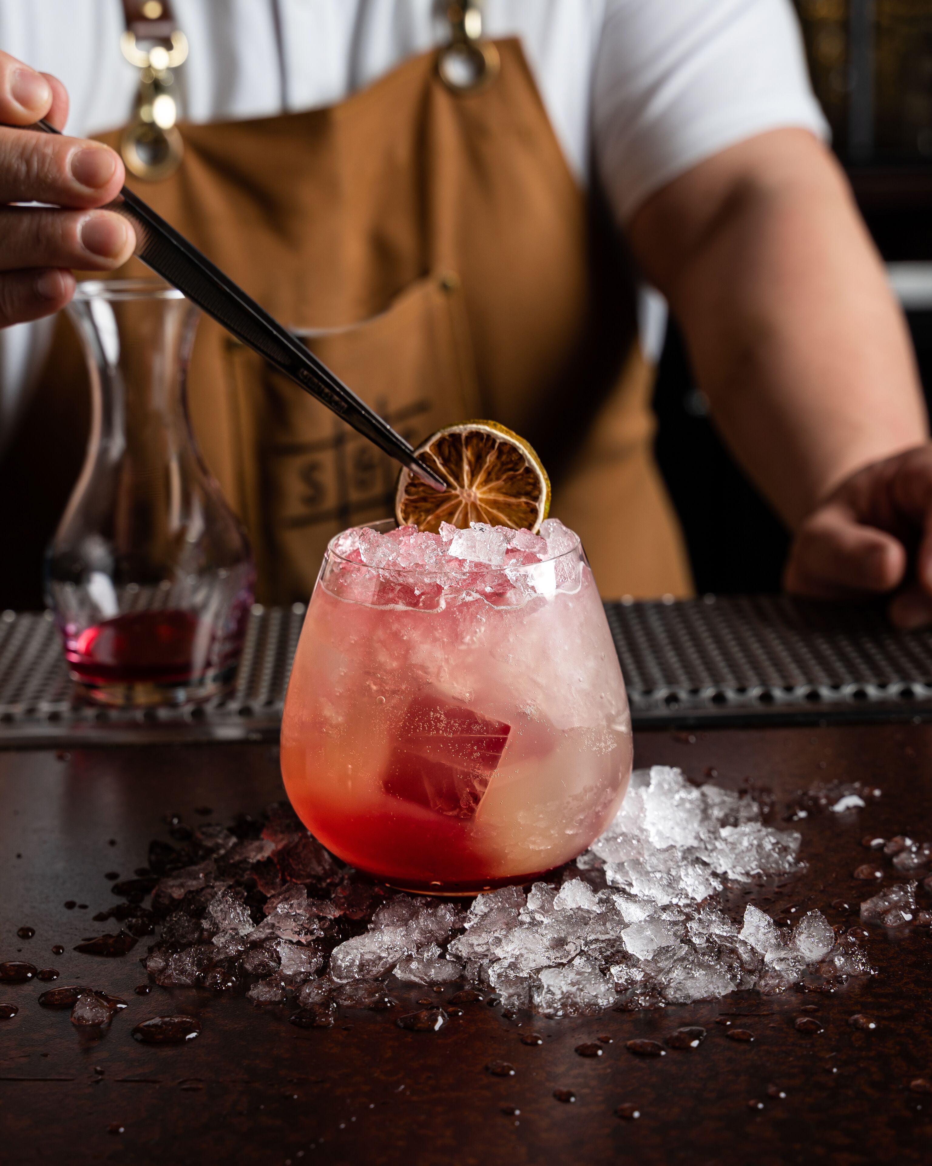 A bartender preparing a cocktail with ice and a slice of citrus garnish.