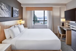 Habitación de hotel con una cama grande, un escritorio con silla, televisión y ventana con vista a las montañas.