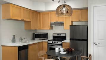A compact kitchen with wooden cabinets, a stainless steel refrigerator, a microwave, an oven, and a dining table with chairs.