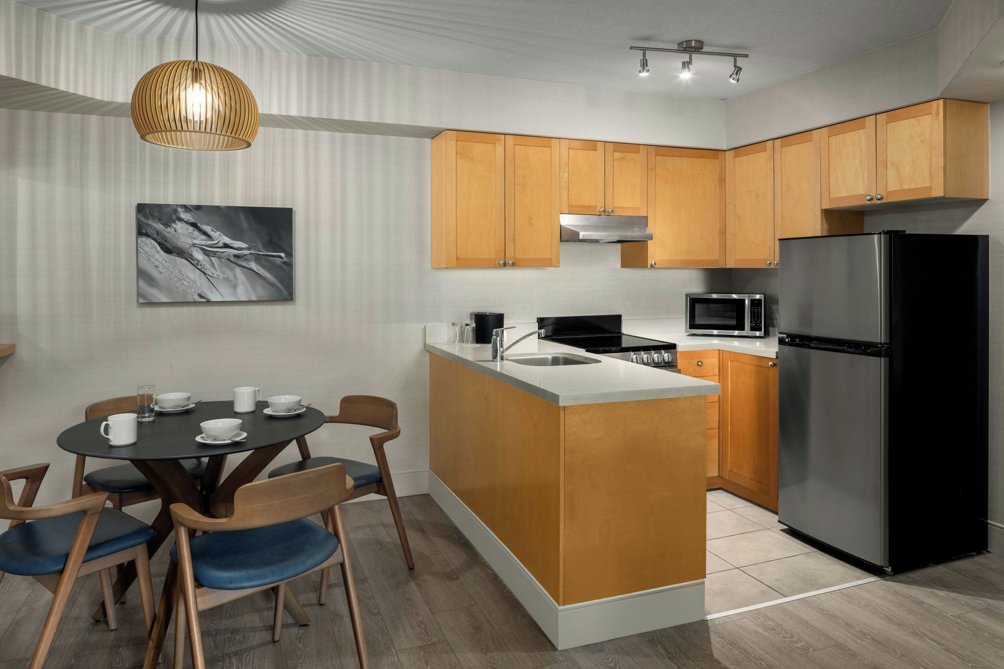 A modern kitchen with wooden cabinets, a black refrigerator, a microwave, and a dining area with a table and chairs.