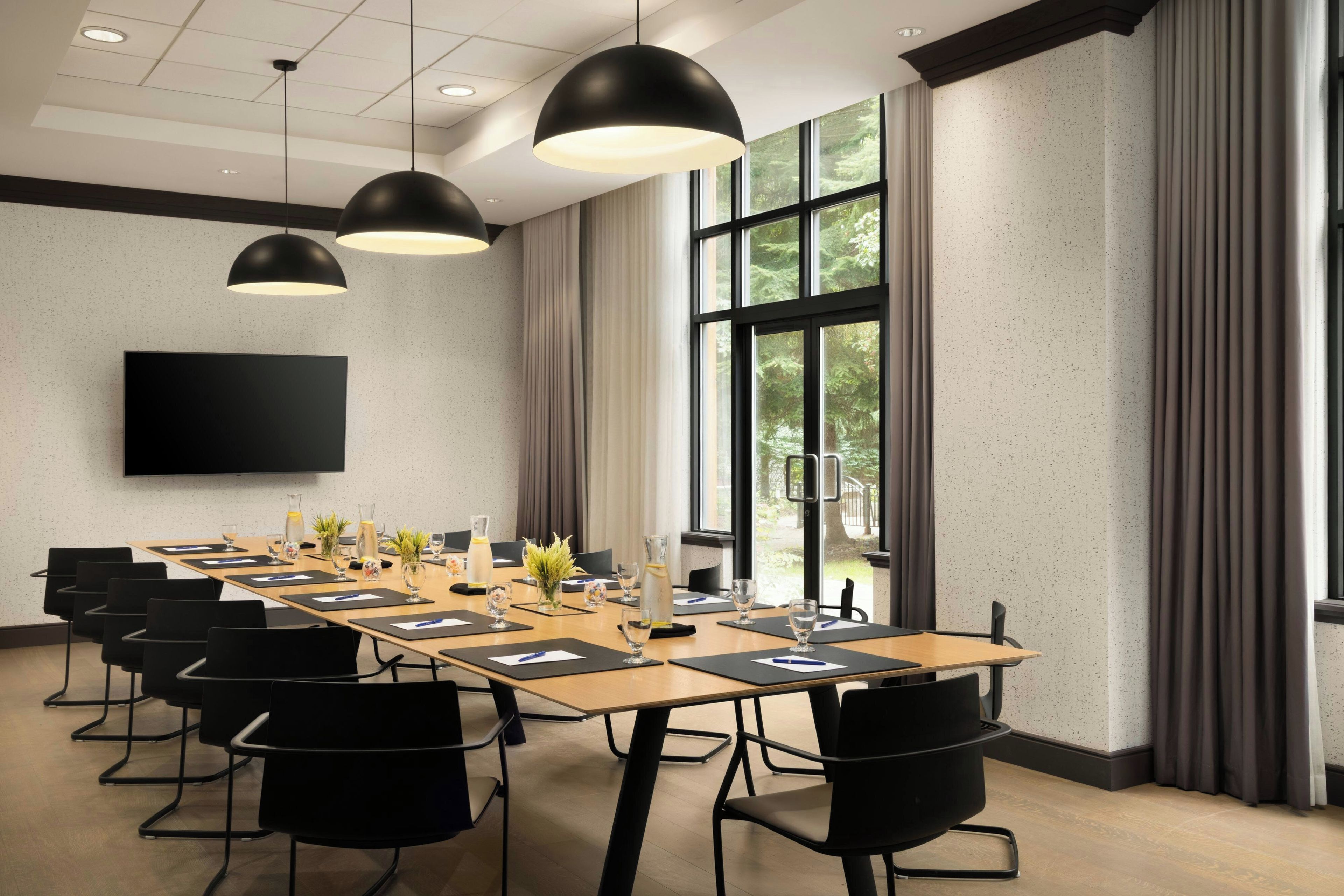 A conference room with a long table, black chairs, and pendant lighting.