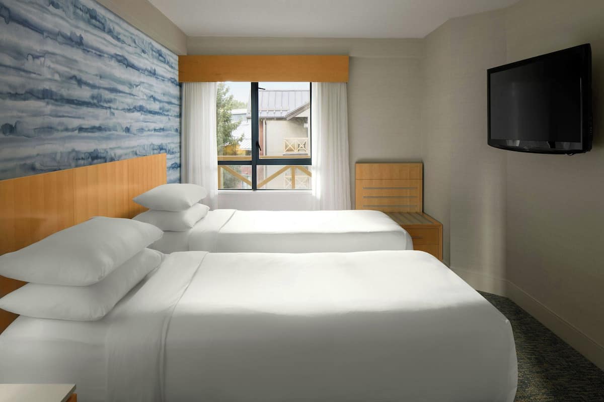 A hotel room with two beds, a TV, a window with curtains, and a view of the outside.