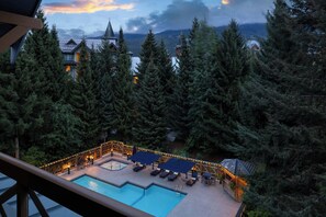 A pool area with lounge chairs and umbrellas, surrounded by tall trees and a mountain backdrop.