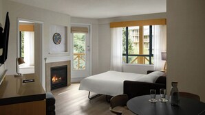 Una habitación de hotel con una cama, un escritorio con lámpara, una chimenea y una ventana con vistas a edificios.