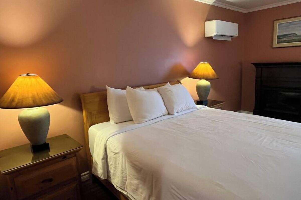 Habitación de hotel con cama, dos lámparas de noche, una mesita de noche, aire acondicionado de pared y chimenea.