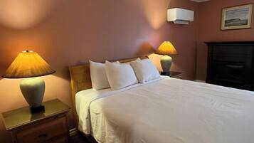 A hotel room with a bed, two bedside lamps, a nightstand, a wall-mounted air conditioner, and a fireplace.