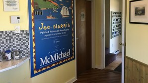 Ein Flur mit einem Poster der Kunst von Joe Norris, einem Thermostat, einer Steckdose und einer Tür zu einem anderen Raum.