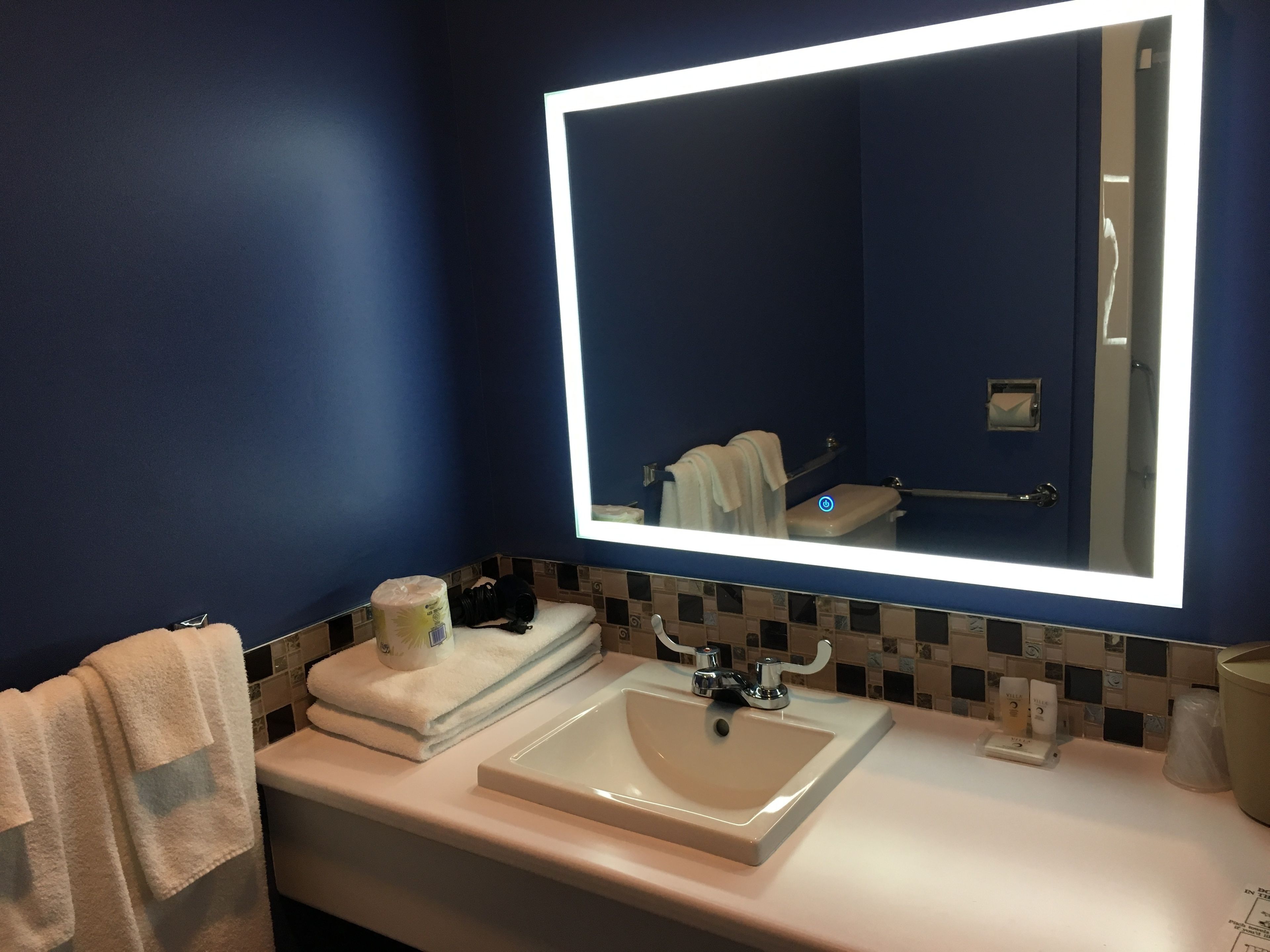 Une salle de bain avec un grand miroir, un lavabo blanc et des murs bleus.