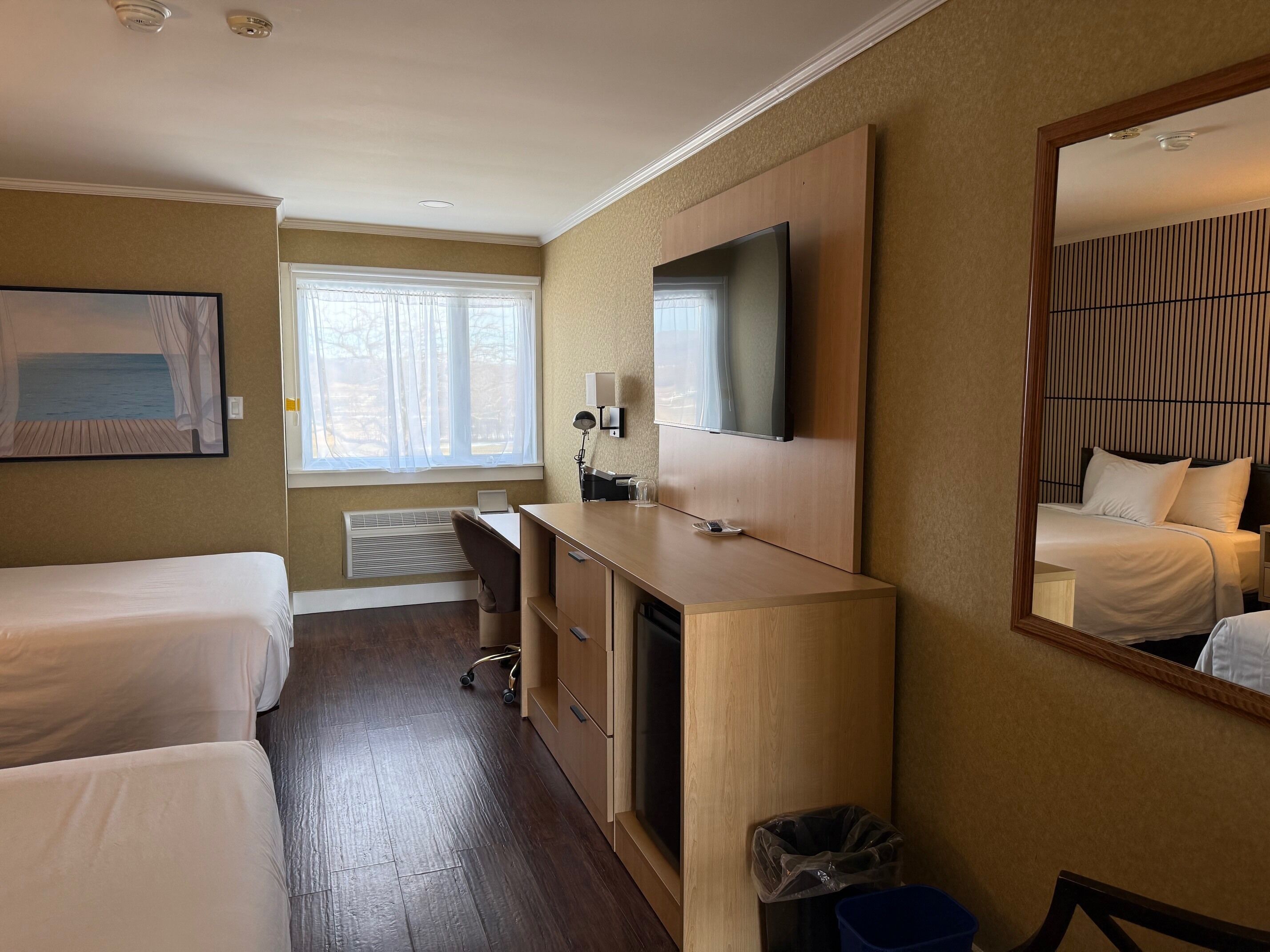 Hotellihuone, jossa on kaksi sänkyä, työpöytä, televisio ja suuri peili.