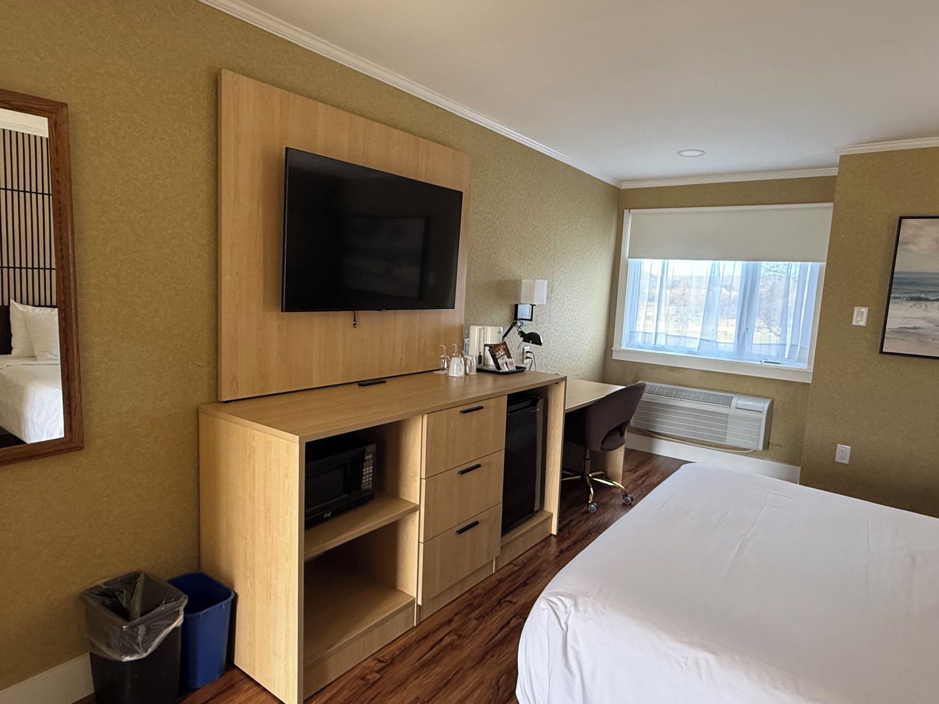 Een hotelkamer met een bed, een bureau, een televisie, een raam en een prullenbak.