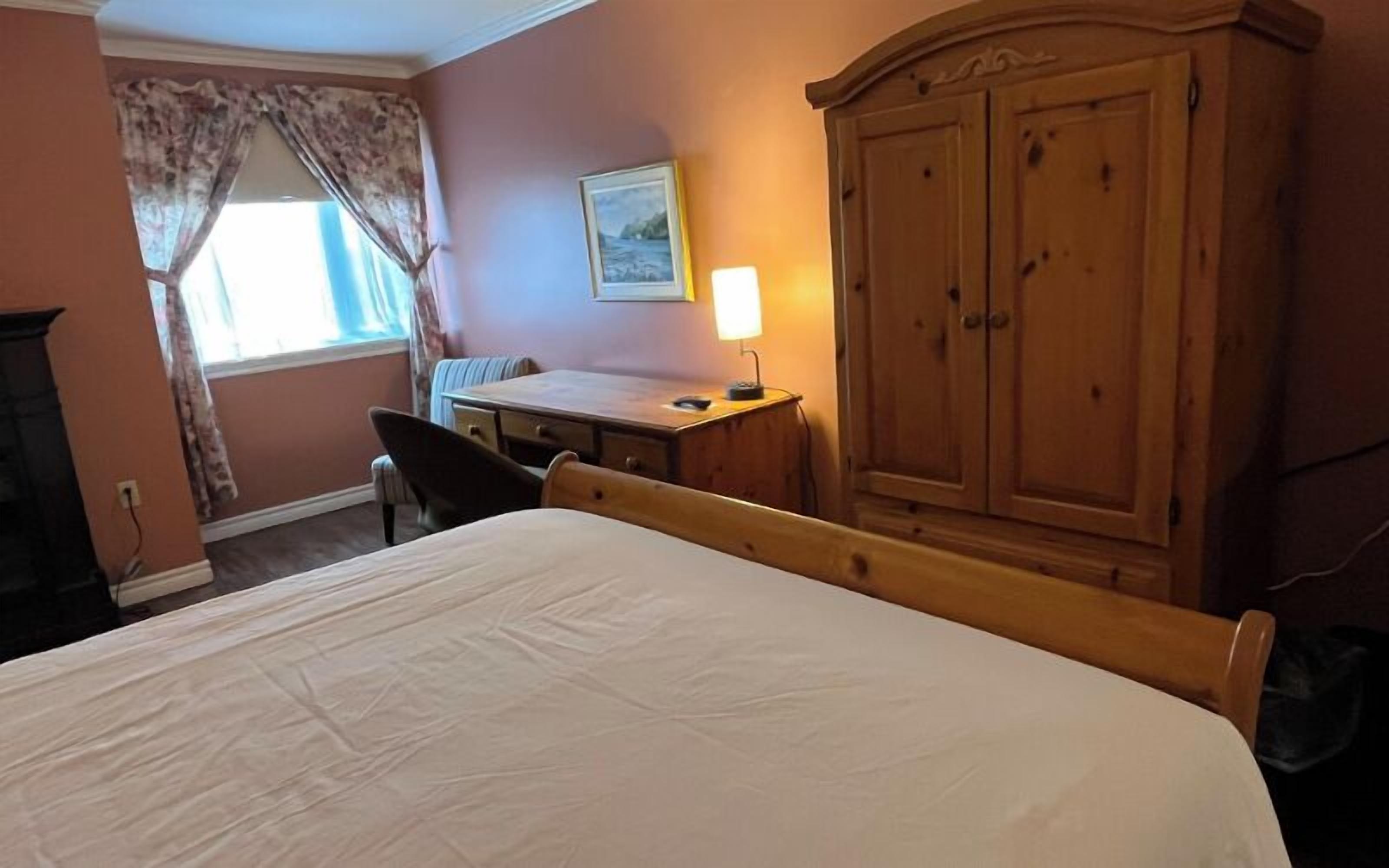 Una habitación de hotel con cama, escritorio, silla, armario y ventana con cortinas.