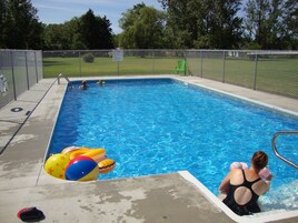 A swimming pool with a fenced area, a lifeguard sign, and a person in a swimsuit.
