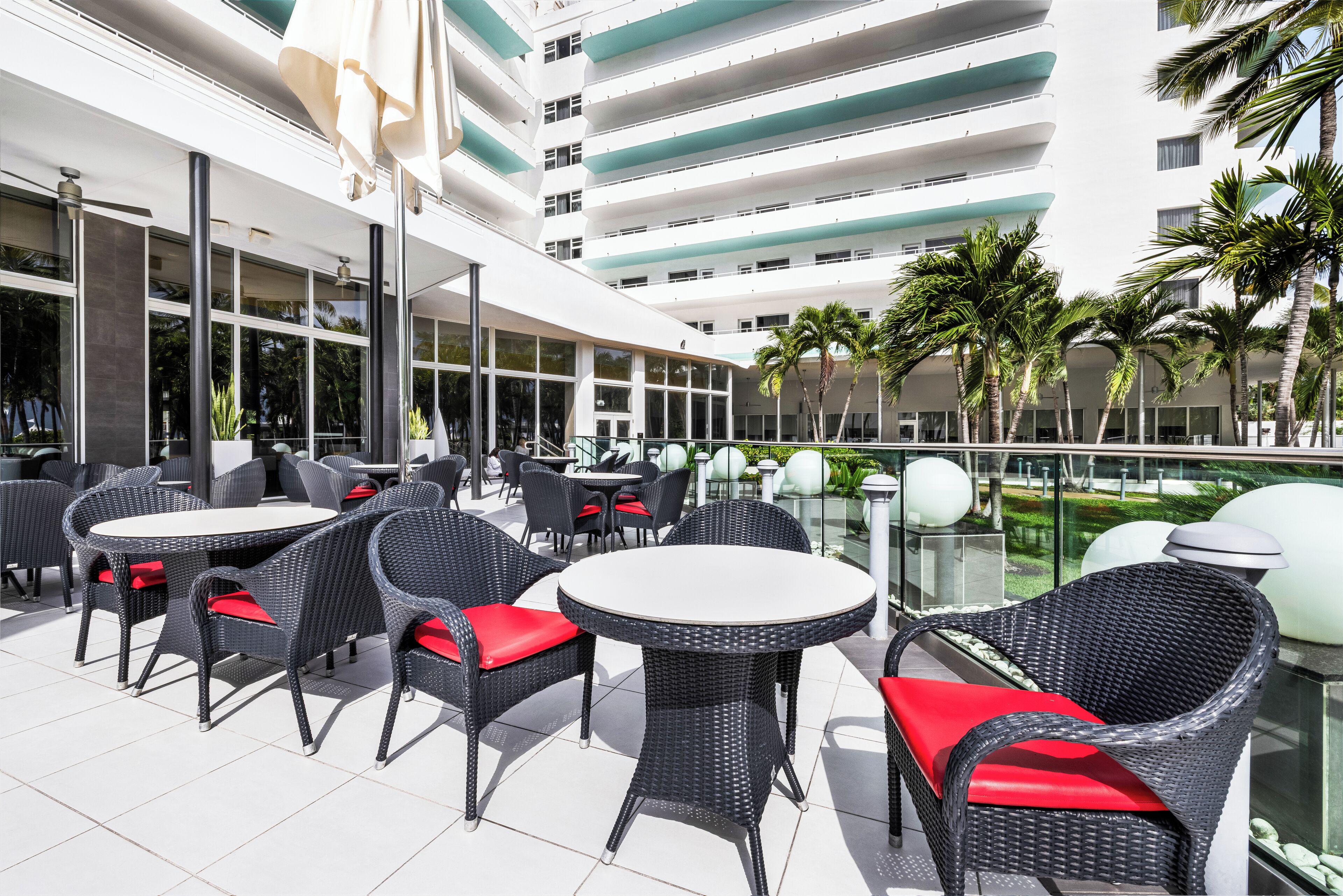 Eine Außenpatio-Terrasse mit Korbmöbeln und roten Kissen, mit Blick auf einen Pool und Palmen.