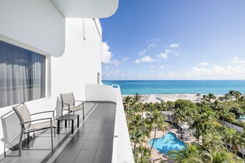 A grand piano in a lobby with a stage, a bar area with drinks, and a seating area with chairs. at Hotel Riu Plaza Miami Beach