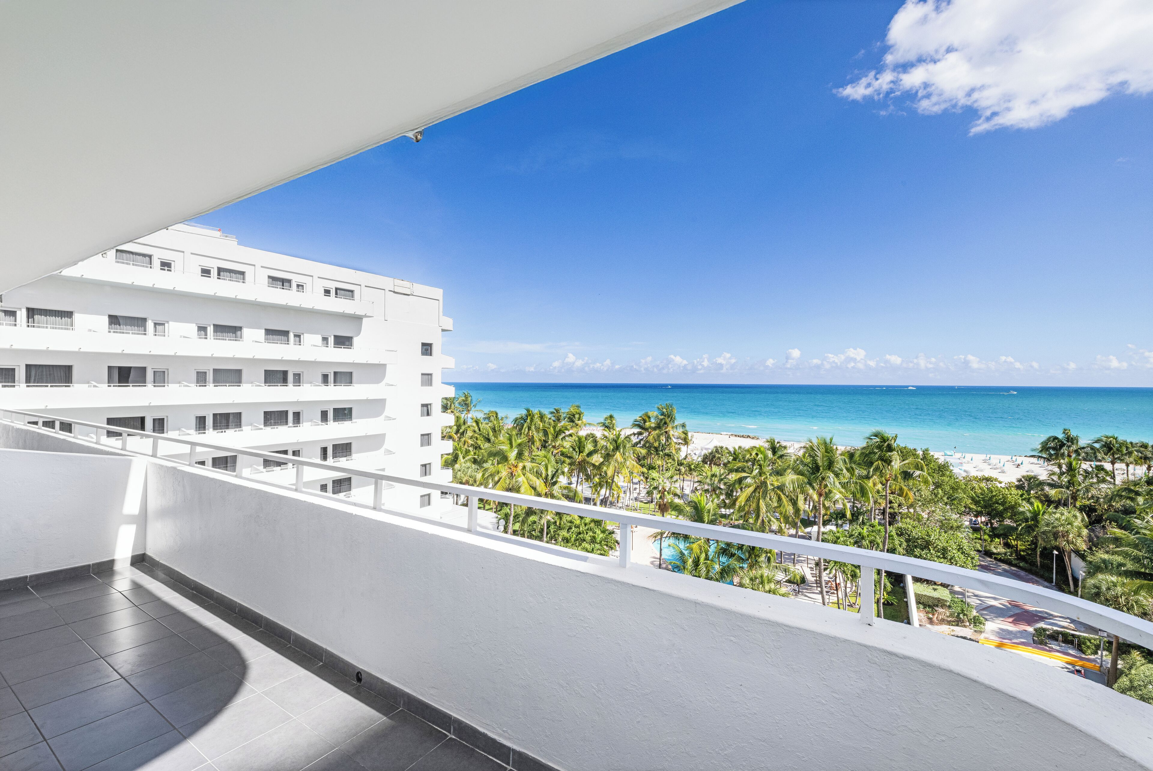 A balcony with a view of a beach, palm trees, and a clear blue sky.