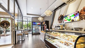 A modern cafe with a glass display case filled with pastries and a TV screen above it. - Hotel Riu Plaza Miami Beach (Miami Beach)